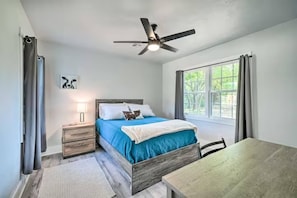 Een slaapkamer met een bed, nachtkastje, lamp, raam en plafondventilator.
