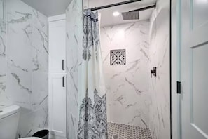 Un baño con paredes de mármol, una ducha con cortina decorada y un pequeño azulejo ornamental en la pared.