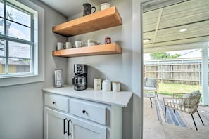 Una cocina con armarios blancos, una cafetera y estantes con tazas y frascos.