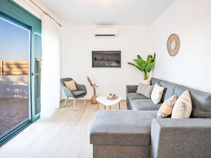 A modern living room with a grey sofa, a small round table, a chair, a potted plant, and a television on the wall. - Gemini Villas- Harmony Villa by Interhome (Rhodos City)