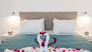 Ein ordentlich bezogenes Bett mit weißen Kissen, einer türkisfarbenen Tagesdecke und Deko-Schwanen aus Handtüchern mit Blumen.