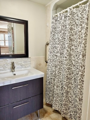 Une salle de bain avec un lavabo blanc, un meuble sombre et un rideau de douche orné d’un motif floral.