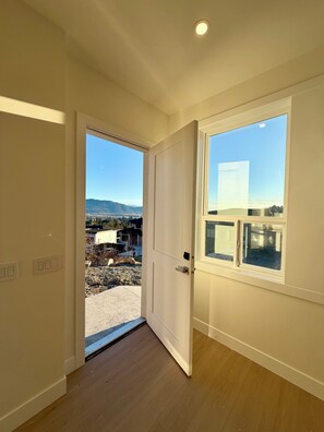 Ein Zimmer mit Holzboden, einer weißen Tür und einem großen Fenster mit Blick auf eine Wohngegend und Berge.