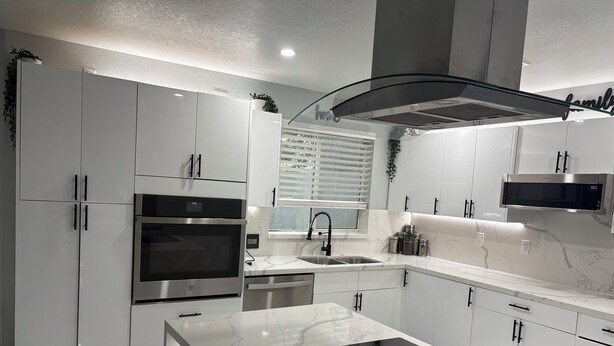 Une cuisine moderne avec des meubles blancs, un four encastré, un four à micro-ondes, un évier et un grand îlot central doté d’une plaque de cuisson.