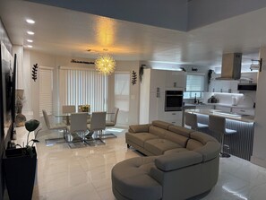 A modern living room with a sofa, dining table, and chairs, a kitchen area with cabinets and appliances, and a decorative light fixture. - Pretty cozy house with 4 bedroom in northwest Las Vegas, single family home (Las Vegas)