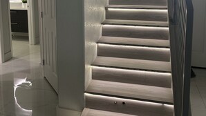 Un escalier avec une rampe, une porte avec un interrupteur et une fenêtre avec des stores.