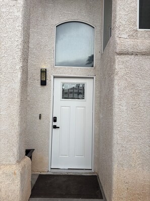 A white door with a small window above it, a keypad lock, and a doormat at the entrance. - Pretty cozy house with 4 bedroom in northwest Las Vegas, single family home (Las Vegas)