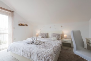 Ein Schlafzimmer mit einem großen Bett, einem Nachttisch mit Lampe, einem Sessel und Wanddeko.