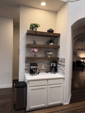 A kitchen with white cabinets, two coffee makers, and shelves with plants. -     Corporate Friendly Frisco Home Fast WiFi Office Near Major Headquarters (Frisco)