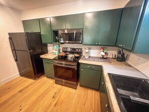 Eine kleine Küche mit Kühlschrank, Herd, Mikrowelle und grünen Schränken.