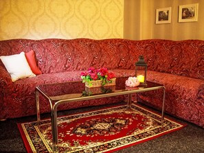 A red patterned sofa with a cushion, a glass coffee table with a red rug, and a wall with two framed pictures. - Herlíkovice by Interhome (Vrchlabi)