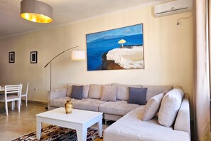 A modern living room with a sofa, a coffee table, a lamp, and a painting of a beach scene. - Happy Stay Vincent - 270 /w Sea View Balcony, Sarandë, Albania (Sarandë)