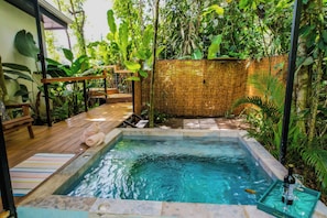 Un jacuzzi rodeado de exuberante vegetación, una terraza de madera y un muro de piedra.