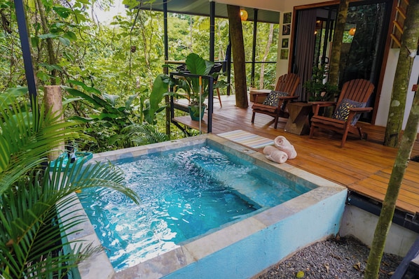 A hot tub surrounded by lush greenery, wooden deck chairs, and a view of the forest. - Tree House La Fortuna w/Jacuzzi (La Fortuna)