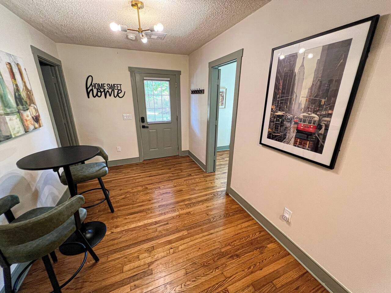 A hallway with wooden flooring, a dining area with chairs and a table, a door with a window, and a framed picture on the wall.