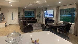 Uma sala de estar com sofá, mesa de jantar, televisão e uma janela grande.