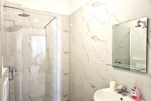 A modern bathroom with a glass shower enclosure, a white sink with a mirror above it, and a marble-patterned wall. - Holiday Apartment With Sea View - 180, Sarandë, Albania (Sarandë)