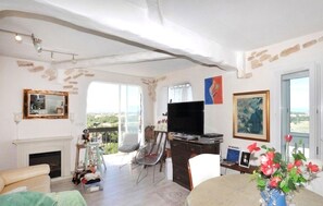 A living room with a fireplace, a television, and a dining area with a table and chairs. - Appartement vue panoramique (Perpignan)