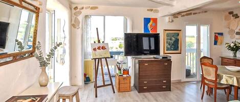 Una habitación con televisor, un cuadro, una mesa de comedor y una silla.