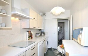 A compact kitchen with a glass-top island, built-in spice rack, and a washing machine. - Appartement vue panoramique (Perpignan)