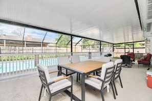 Eine überdachte Terrasse mit Blick auf einen Pool, Sitzgelegenheiten im Freien und einem Grill.
