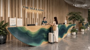 Una recepció amb un disseny ondulat, una paret de fusta amb llistons verticals i un cartell que diu 'THE SEA & SAND RESIDENCES'.