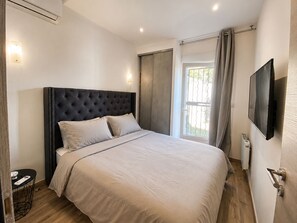 A modern bedroom with a large bed, a flat-screen TV, and a window with curtains. - Cozy Little House Between Monaco the Beach (Cap d'Ail)