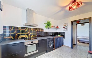 A compact kitchen with a stove, oven, and washing machine, a plant, and a door leading to a sleeping area. - 2 bedroom beautiful apartment in Lachamp Raphael (Lachamp Raphael)
