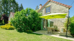 Ein Steinhäuschen mit einer grünen Tür, einer Terrasse mit Tisch und Stühlen und einem gelben Sonnenschirm.