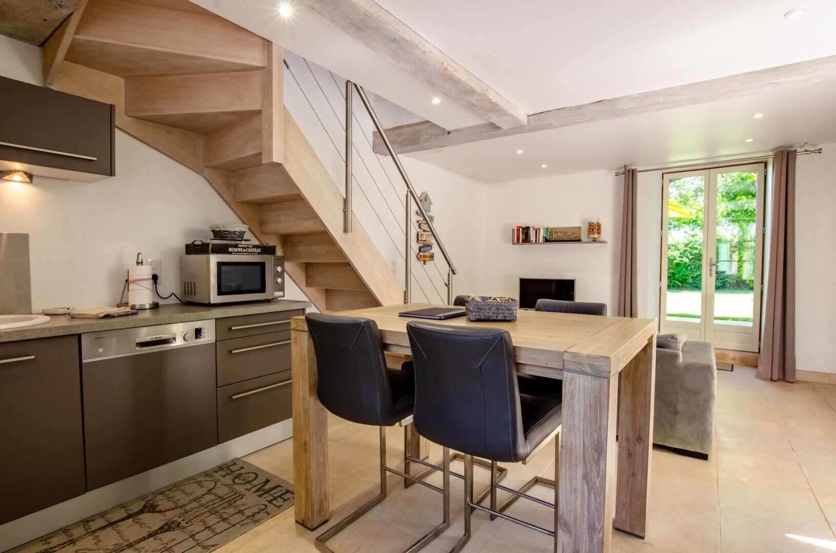 Una cucina moderna con una scala in legno, elettrodomestici integrati e un'area pranzo con due sedie.