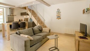 Ein modernes Wohnzimmer mit Sofa, Couchtisch, Fernseher und Küchenzeile mit Treppe.