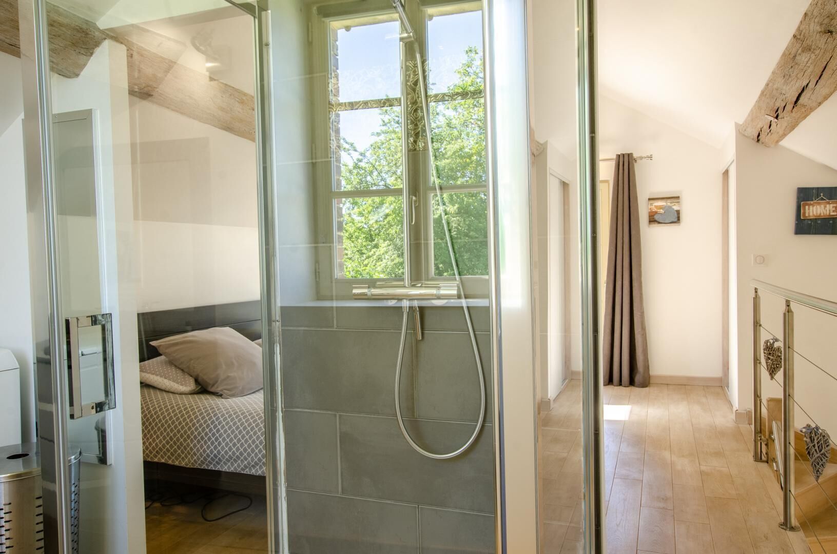Un bagno moderno con box doccia in vetro, un letto con biancheria a motivi decorativi e una finestra ben visibile.
