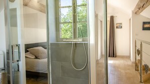 Ein modernes Badezimmer mit Duschkabine aus Glas, einem Bett mit gemusterten Textilien und einem sichtbaren Fenster.
