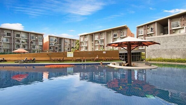 A swimming pool with lounge chairs and umbrellas, surrounded by multi-story residential buildings. - 2 Bedroom Unique Indoor Pool Villa (Bophut)