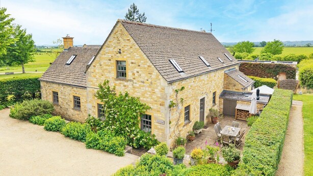 A stone house with a sloped roof, a garden with various plants, and a small outdoor seating area. - Claytons Cottage -  Cotswold Family Retreat near Stow-on-the-Wold (Lower Oddington)
