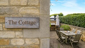 Eine rustikale Steinmauer mit einem Holzschild, auf dem 'The Cottage' steht.