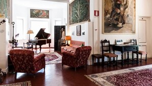 A spacious living room with a grand piano, red upholstered chairs, a large painting, and a dining area with a table and chairs. - Hotel Club i Pini- Residenza d'Epoca (Camaiore)
