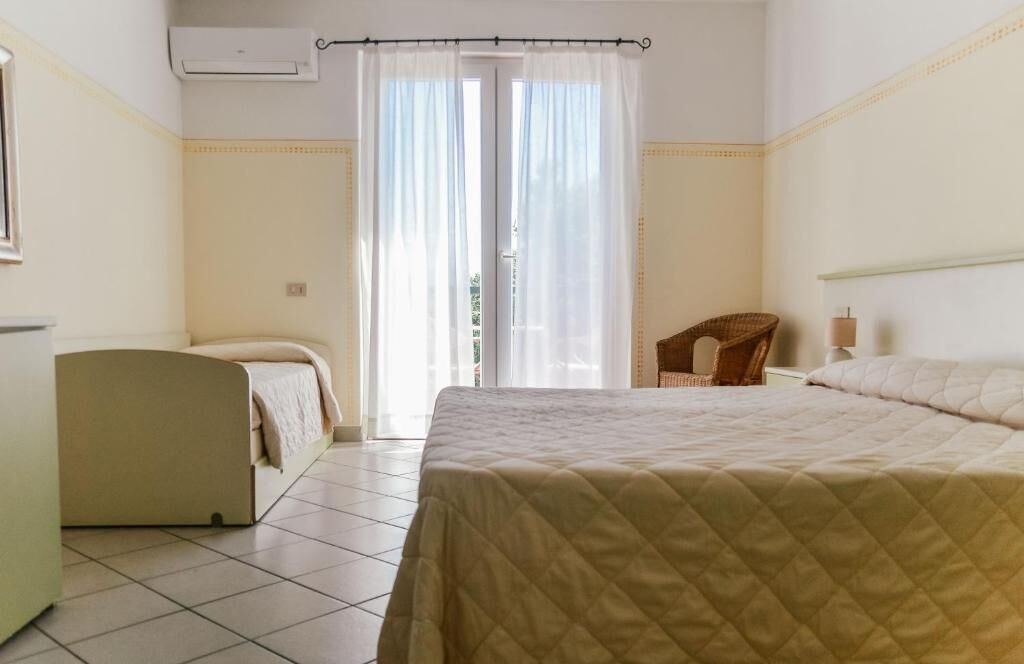 A room with a bed, a chair, a small table, and a window with curtains.