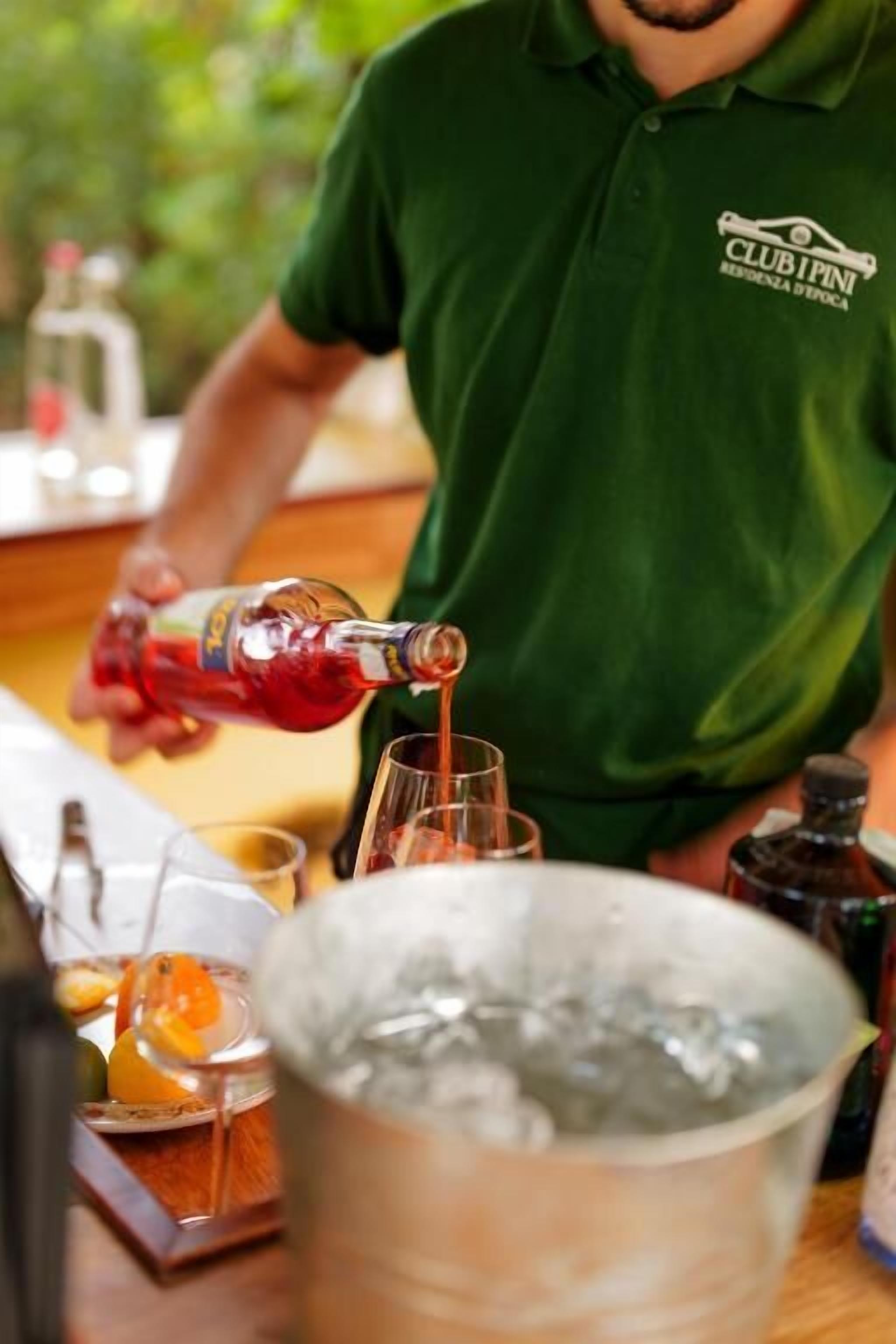 A person pouring a drink into a glass, with a bucket of ice and a tray of food items in the foreground.