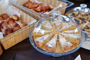 A buffet table with a variety of baked goods, including a covered pie and baskets of pastries.