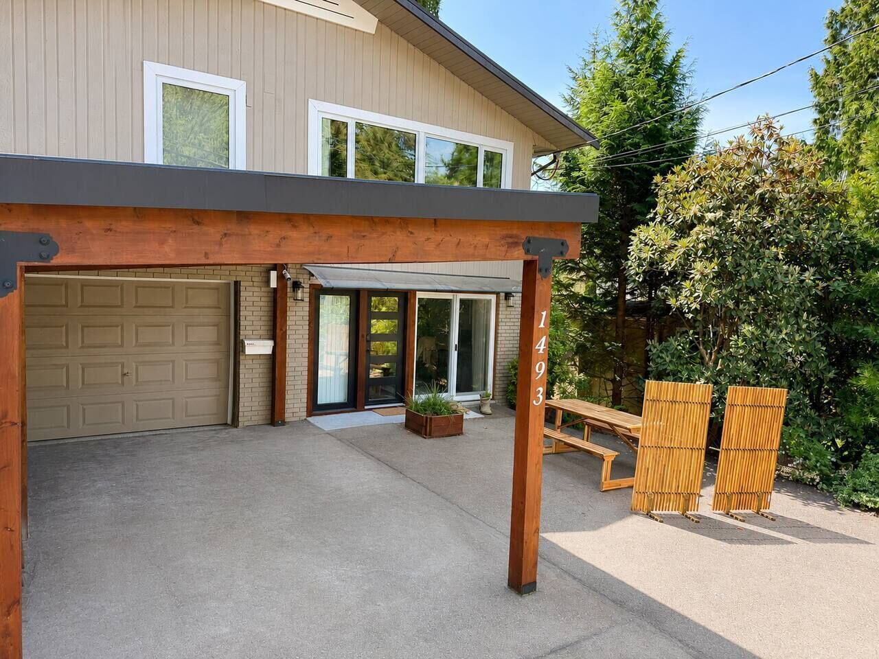 A covered patio area with a garage door, a wooden pergola, and a bench.
