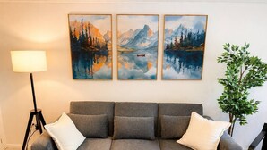 A grey sofa with white cushions, a floor lamp, and a potted plant in a room with a white wall. - Modern North Van Escape with 2BR | BBQ | Workspace (North Vancouver)