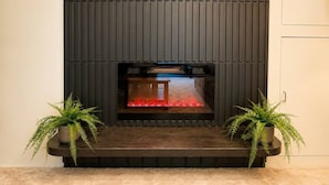 A fireplace with a dark, vertical panel design, flanked by two potted plants. - Modern North Van Escape with 2BR | BBQ | Workspace (North Vancouver)