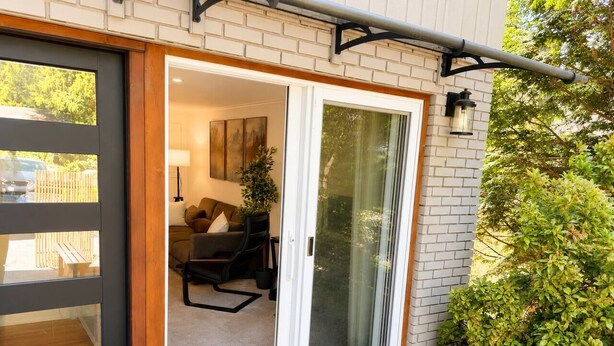 A modern entrance with a sliding glass door, a doormat, and a small potted plant. - Modern North Van Escape with 2BR | BBQ | Workspace (North Vancouver)