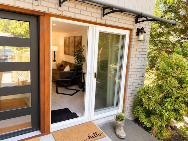 A modern entrance with a sliding glass door, a doormat, and a small potted plant. - Modern North Van Escape with 2BR | BBQ | Workspace (North Vancouver)