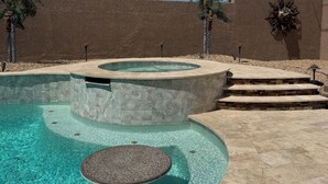 Una piscina con borde de piedra, un jacuzzi y un banco de piedra.