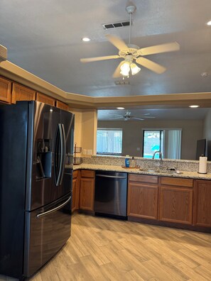 A kitchen with a stainless steel refrigerator, wooden cabinets, granite countertops, a dishwasher, a ceiling fan, and a window with blinds. - Pool & Spa - Boat Parking - 1 Mile to Downtown (Lake Havasu City)