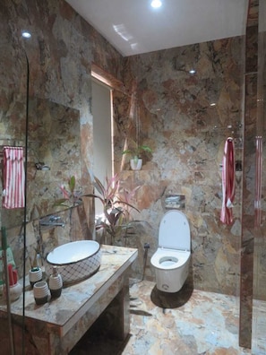 A bathroom with a marble wall, a sink, a toilet, and a shower.