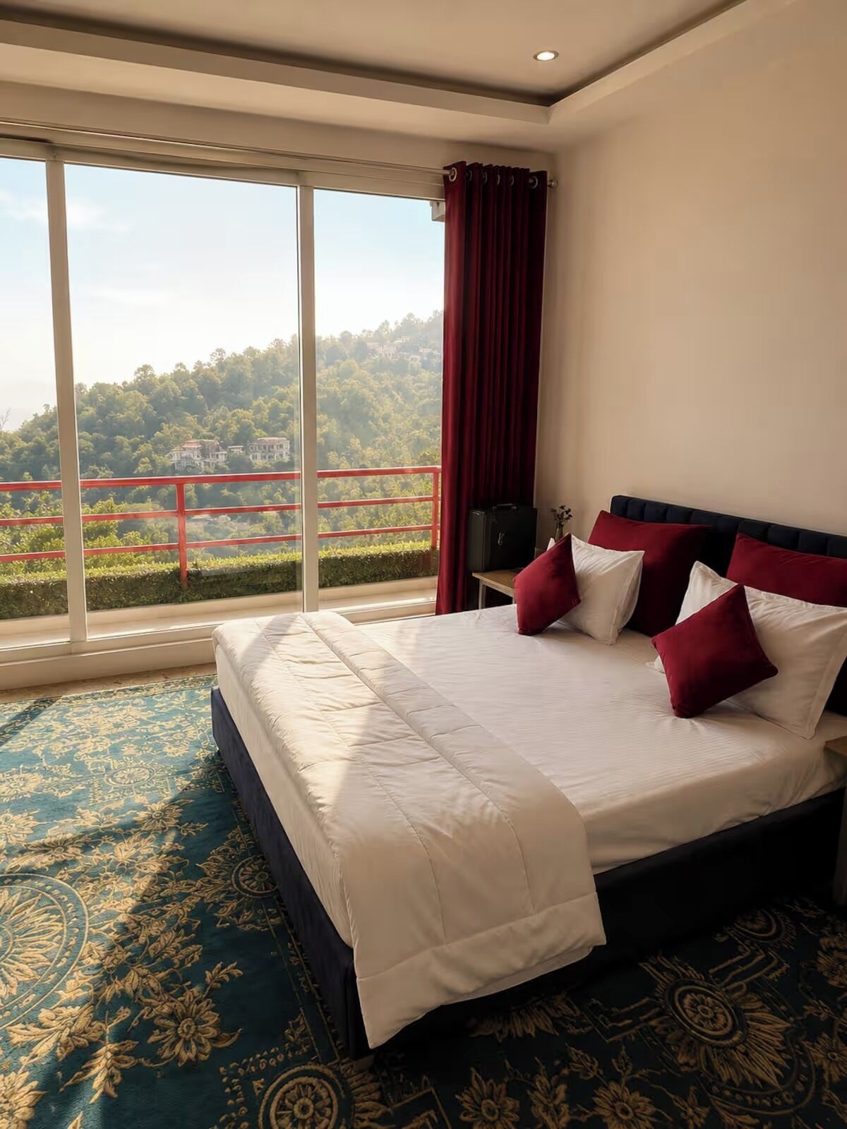 A hotel room with a large bed, a view of a mountainous landscape, and a balcony with a red railing.