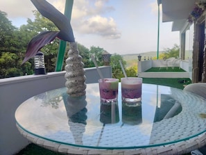 A glass table with two drinks, a decorative object, and a view of greenery and a building.